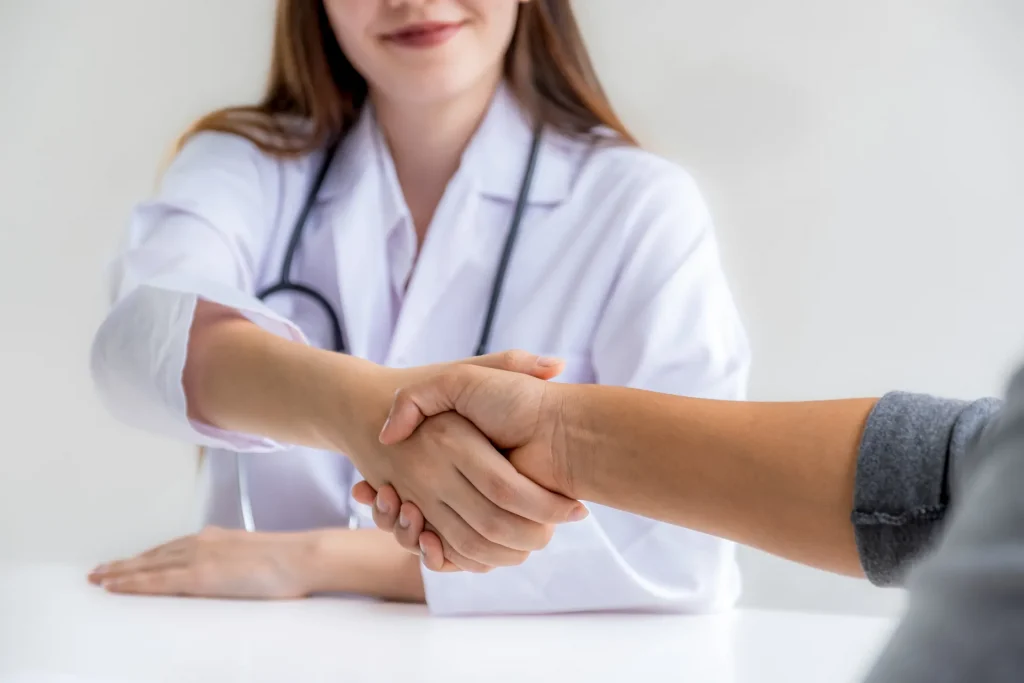 Médico y paciente estrechando manos en consulta, simbolizando confianza y colaboración en el cuidado de la salud.